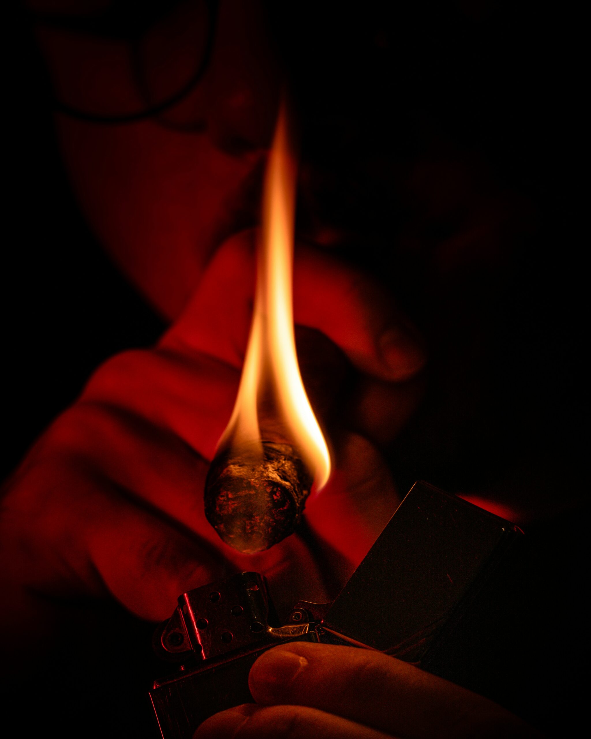 Close-up of a hand holding a lit cigar with smoke swirling